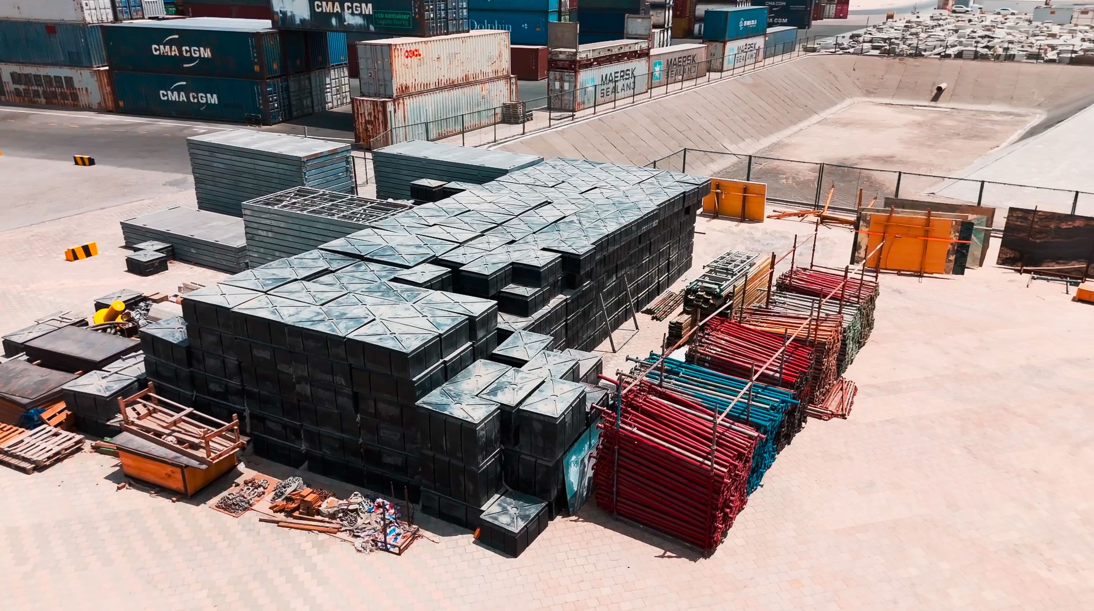 Aerial view of a construction site with neatly stacked metal scaffolding, colorful materials, and geometric patterns conveying order and industrial activity.